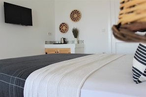 A bedroom with a bed, a TV mounted on the wall, and a kitchen area in the background. - Villamer Hotel Alacati (Cesme)