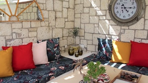 Una habitación acogedora con pared de piedra, un reloj redondo, un sofá con cojines coloridos y una mesita con adornos.