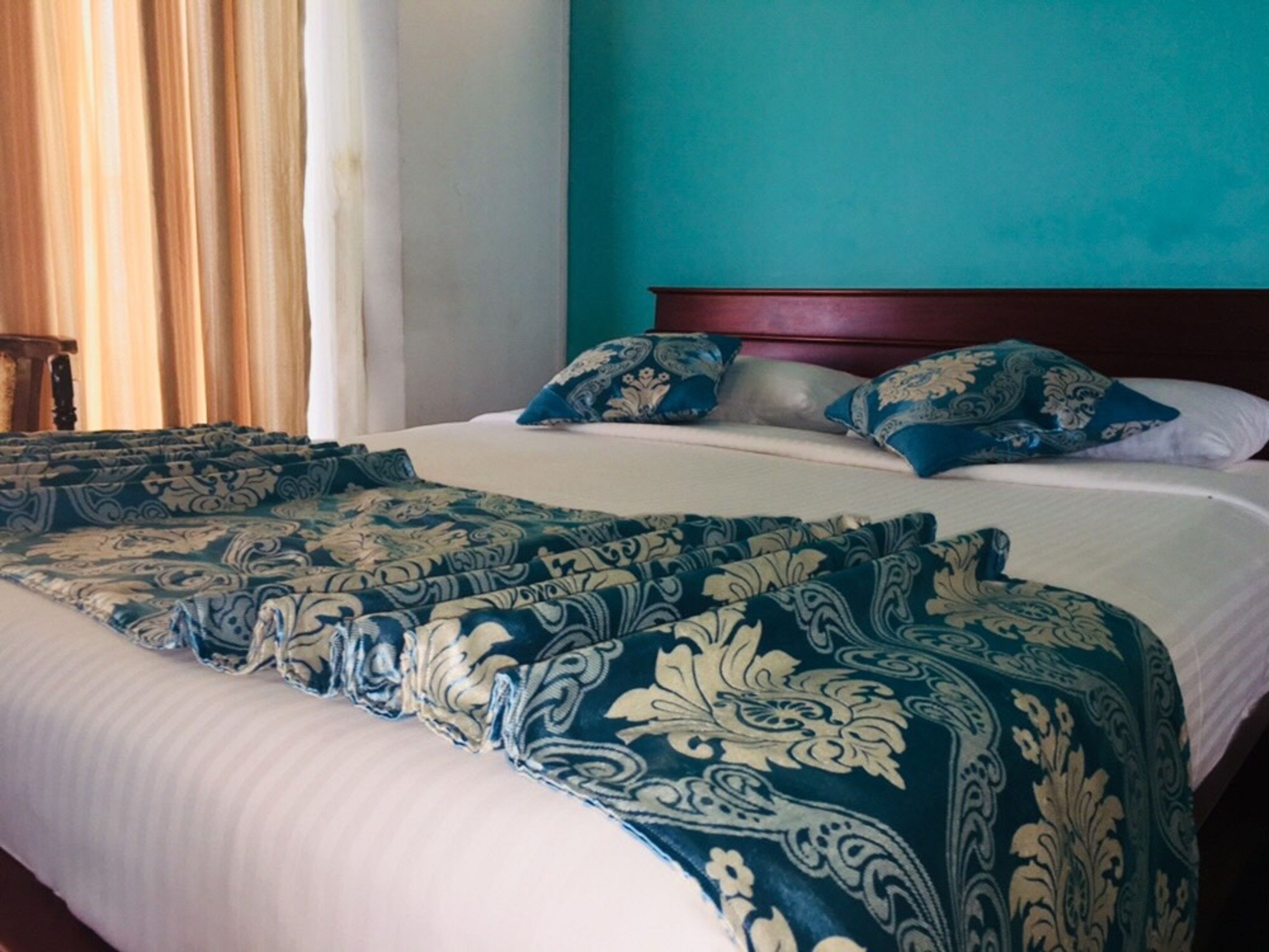 A neatly made bed with a patterned bedspread and pillows, a wooden headboard, and a teal wall.