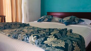 A neatly made bed with a patterned bedspread and pillows, a wooden headboard, and a teal wall.