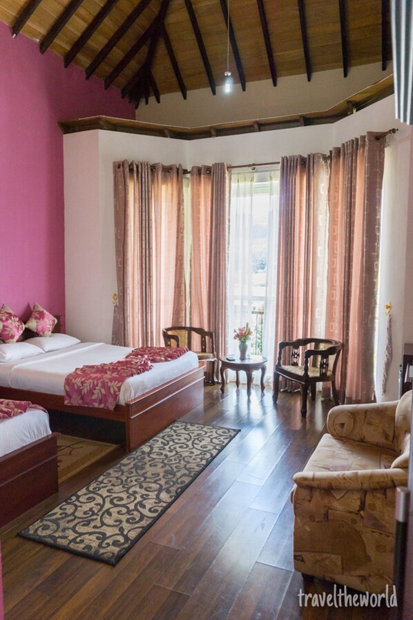 A bedroom with a wooden bed, a sofa, two chairs, a small table, and a window with curtains.