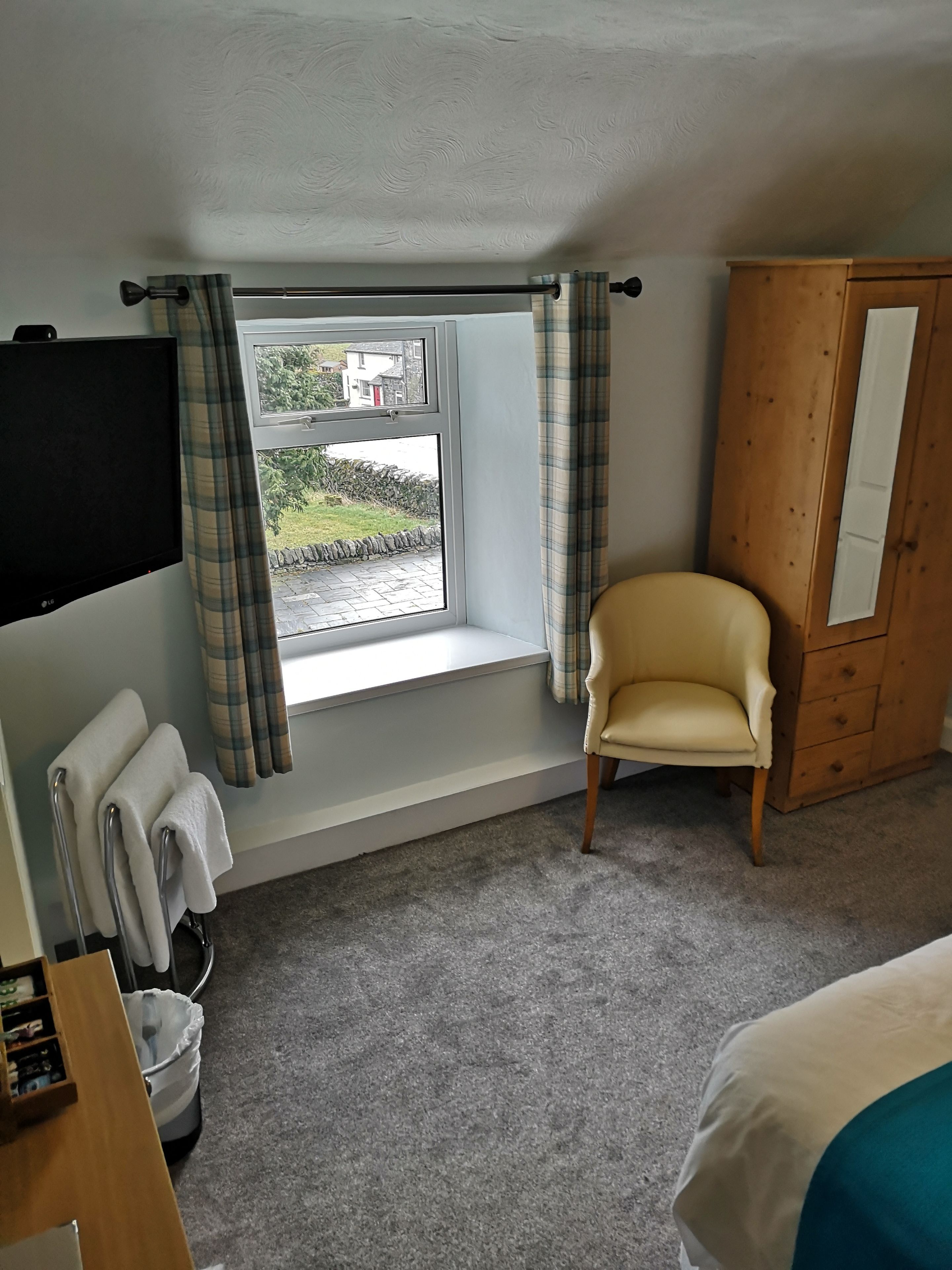 A bedroom with a window, a wooden wardrobe, a chair, a TV, and a radiator.