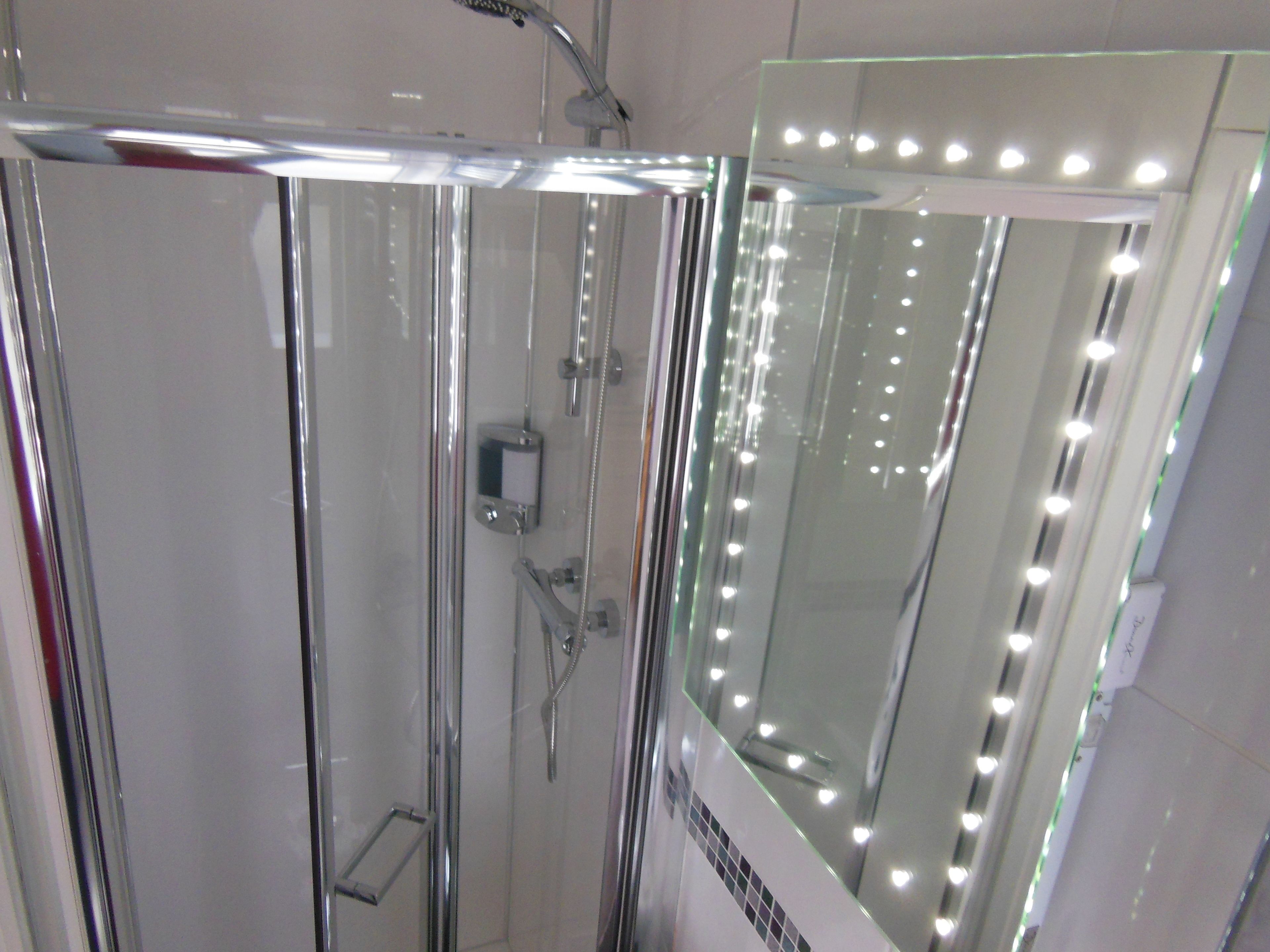 Un box doccia in vetro con soffione a mano e specchio illuminato.