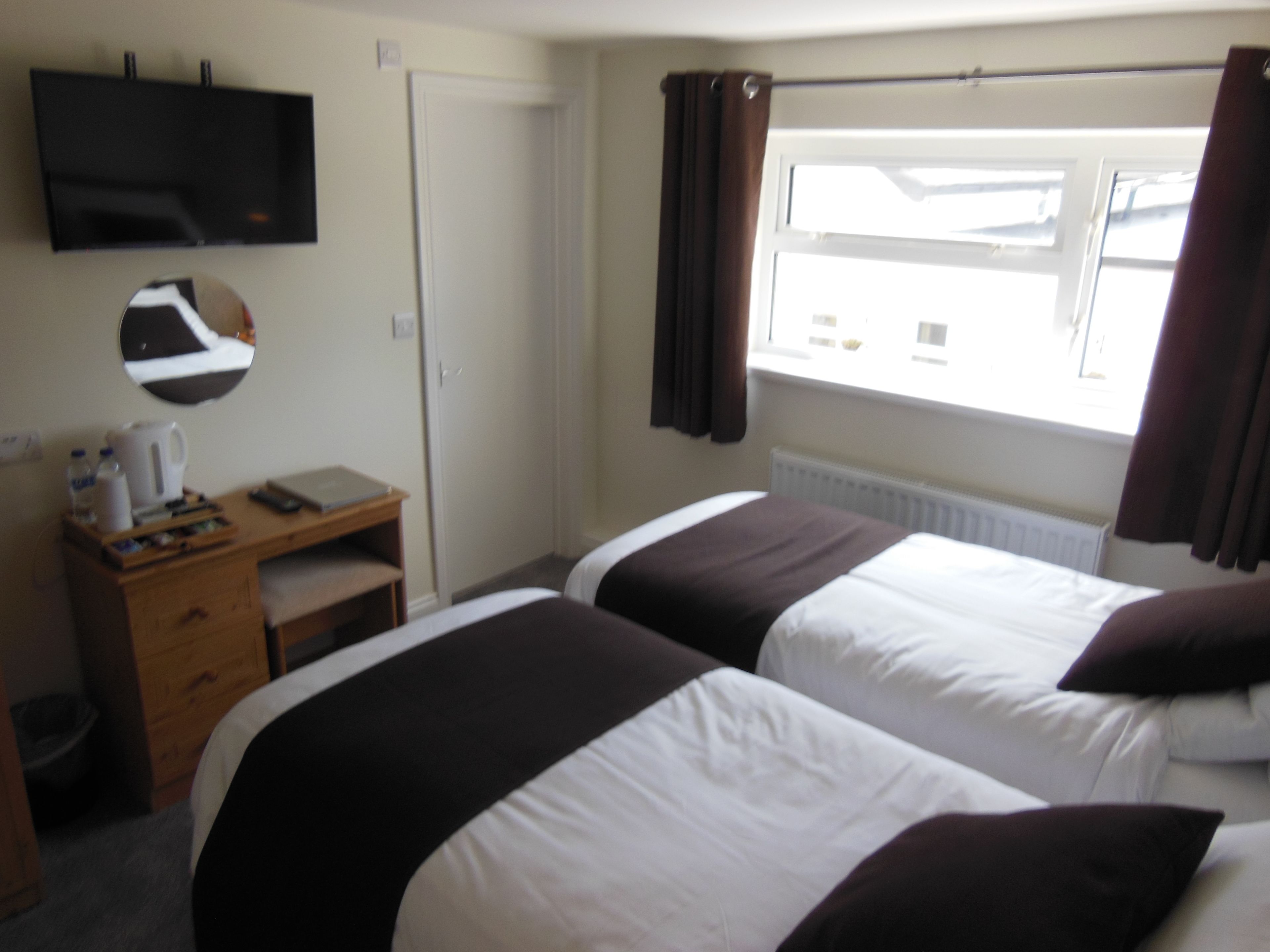 Une chambre d’hôtel avec deux lits, un bureau, un miroir, une télévision et une fenêtre avec des rideaux.