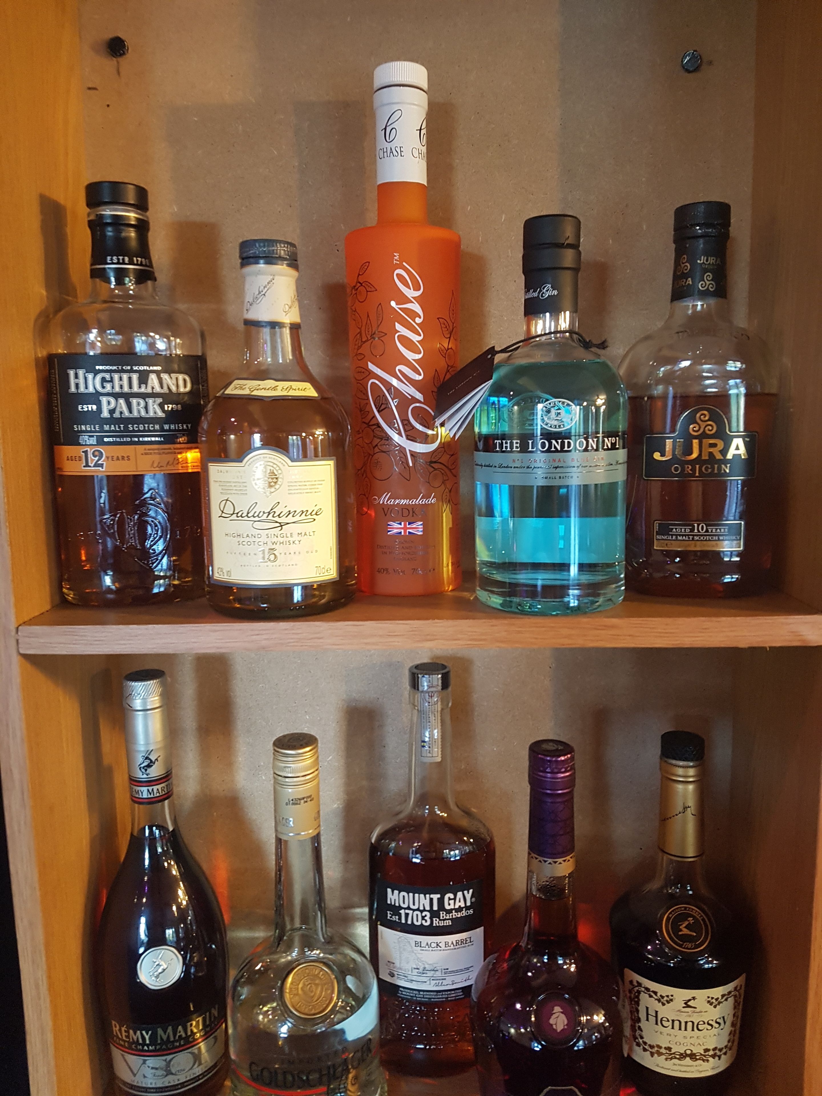Een plank met diverse alcoholische flessen, waaronder whisky, wodka, rum en champagne.