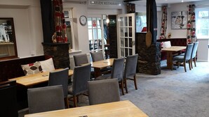 Een restaurantinterieur met meerdere tafels en stoelen, een stenen open haard en een klok aan de muur.