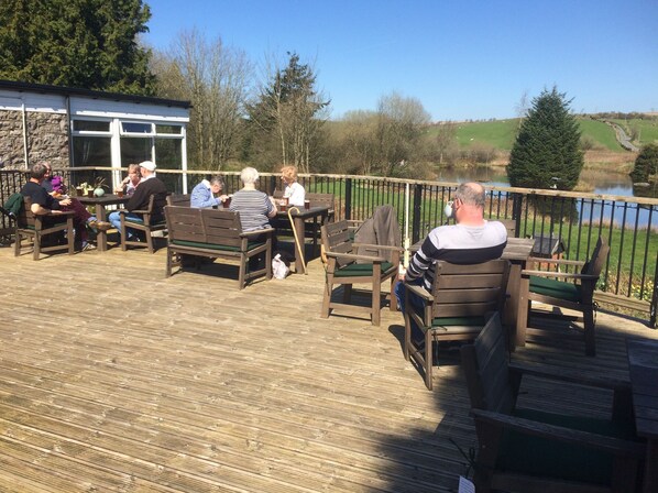 A wooden deck with outdoor seating, a stone building, and a view of a lake and hills. - Y Giler Arms (Betws-Y-Coed)