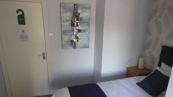 Habitación de hotel con cama, mesita de noche, un cuadro y una puerta con un cartel colgado.