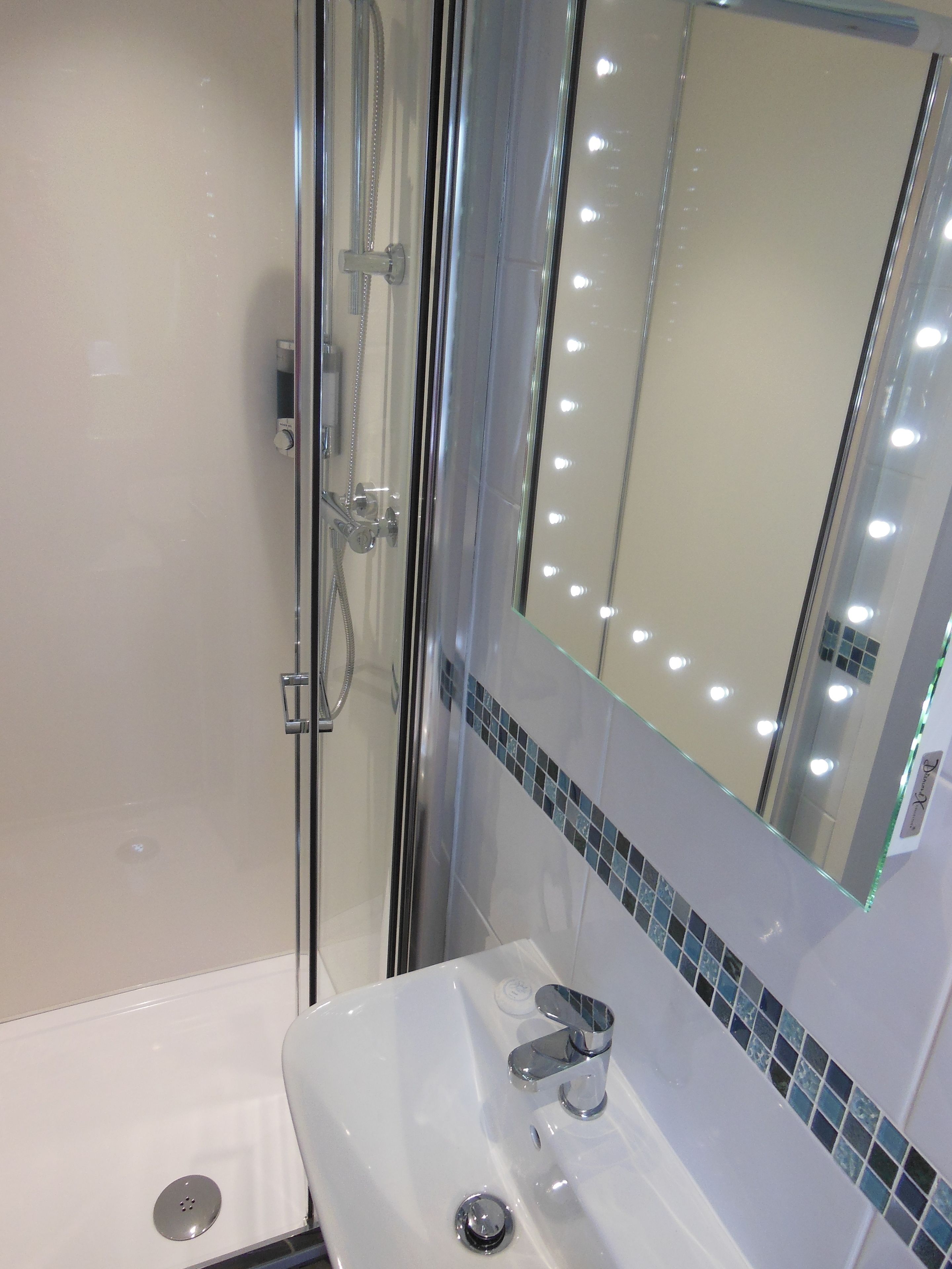 A modern bathroom with a glass-enclosed shower, a white sink, and a mirror with lights.