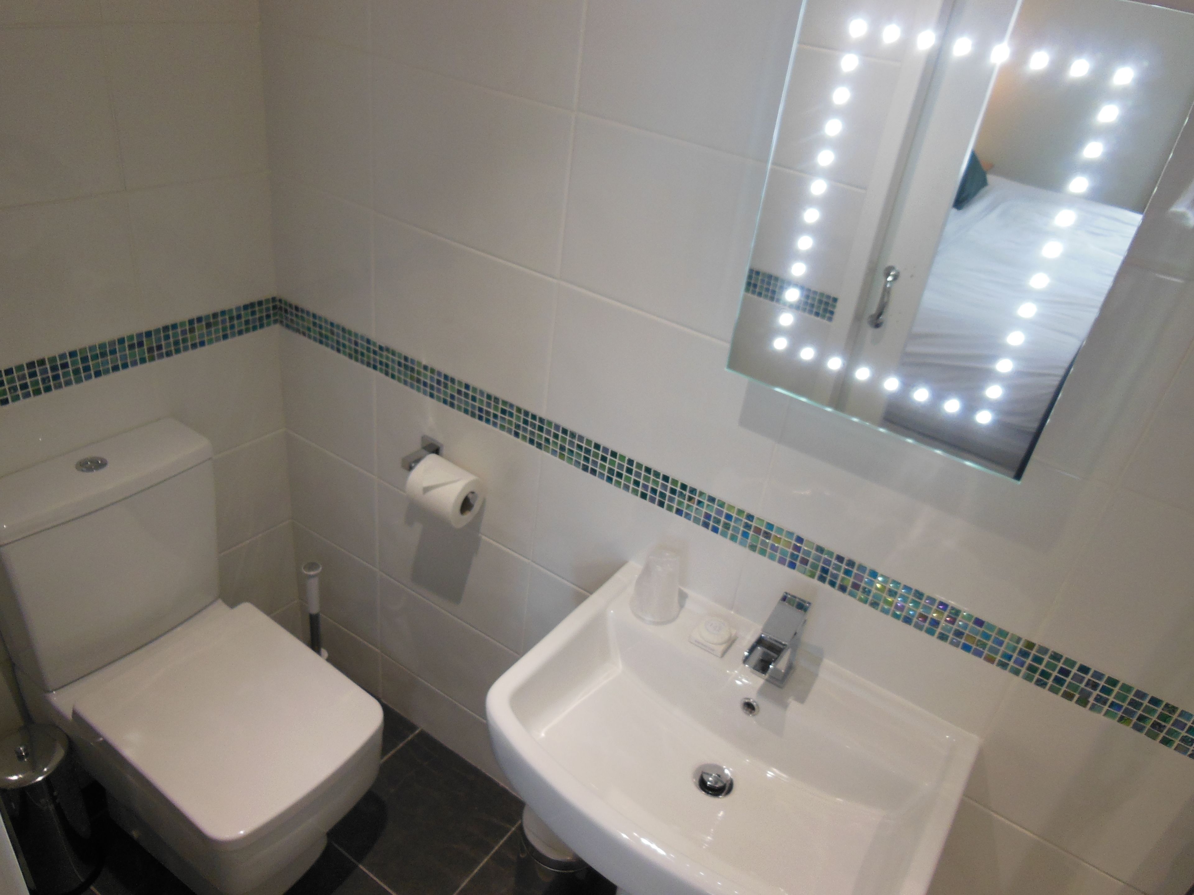 Un baño con inodoro, lavamanos y espejo con iluminación.