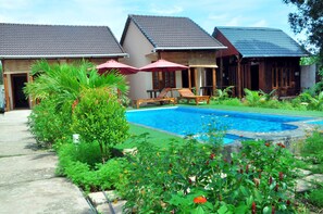 A pool area with lounge chairs and umbrellas, surrounded by lush greenery and a small garden. - Thuy Van Bungalow (Phu Quoc)