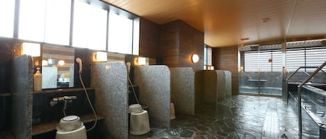 A stone-floored bathroom with multiple sinks and hand dryers.
