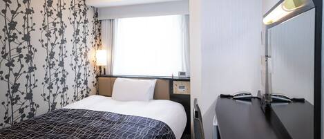 Habitación de hotel con cama, escritorio, silla, lámpara y ventana.