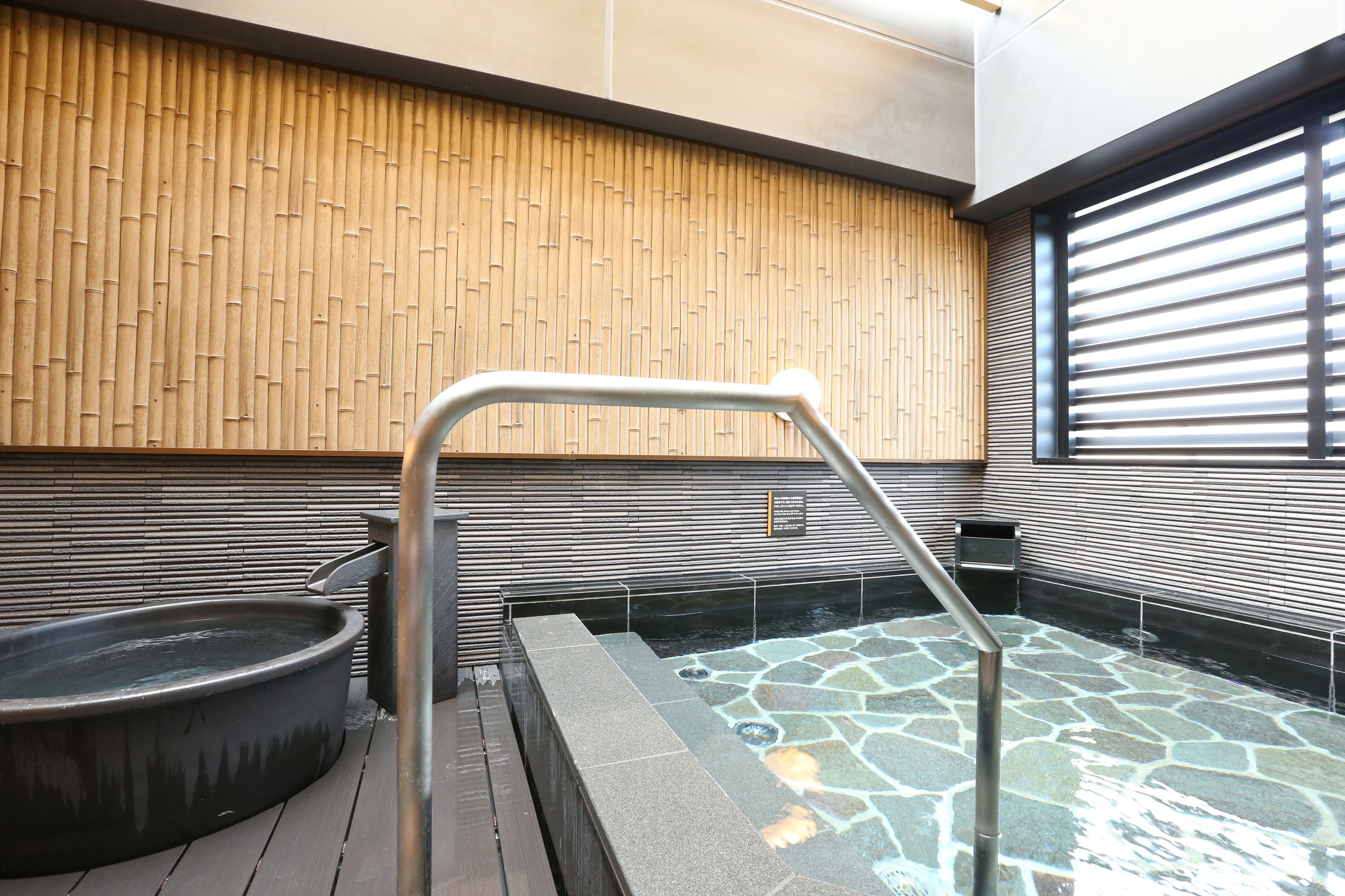 Een moderne spa met een stenen hottub, een houten wand en een metalen leuning.
