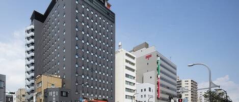 Um hotel moderno com um grande letreiro 'APA HOTEL', situado num cruzamento urbano sob um céu claro.