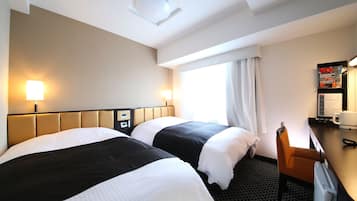 A hotel room with two beds, a desk, a chair, and a window with curtains.