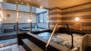 Un área de baños termales con suelo de piedra, paredes de madera y una pared de vidrio.