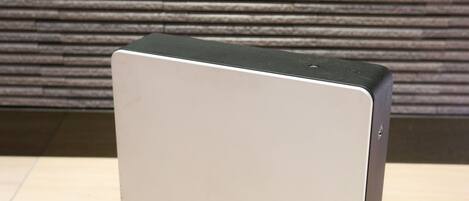 A modern, minimalist air purifier with a sleek design, placed on a wooden floor against a textured wall.