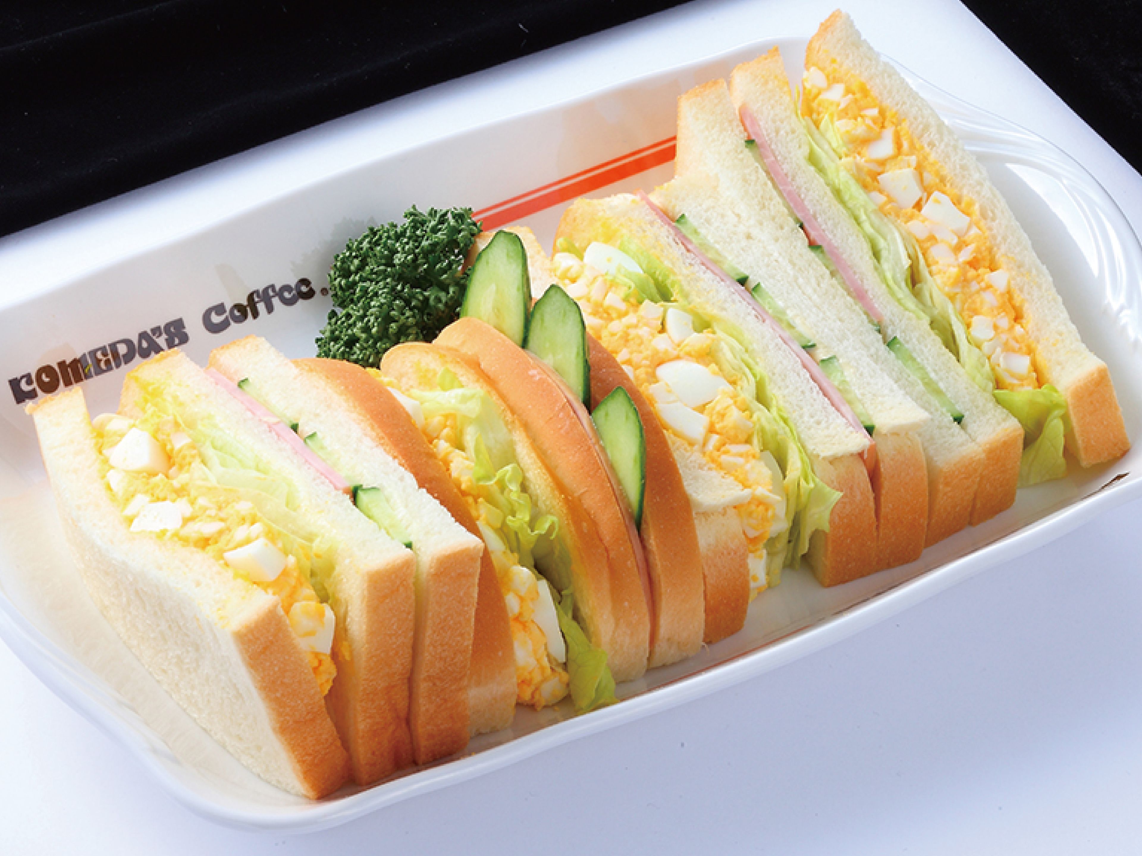 Une assiette rectangulaire blanche sur laquelle se trouve un sandwich coupé en quatre morceaux, garni de laitue, de concombre et d’œuf.