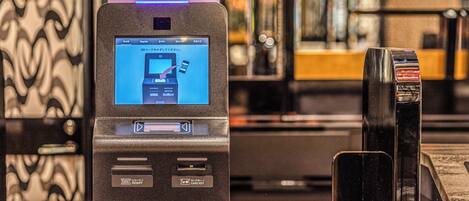 A self-service kiosk with a screen displaying instructions for QR code scanning, a receipt slot, and a card key slot.
