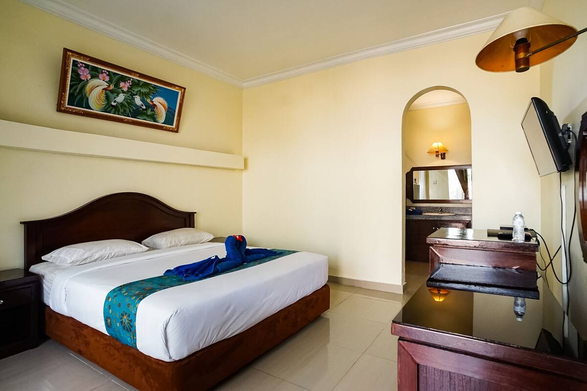 Een hotelkamer met een bed, een bureau, een spiegel en een schilderij aan de muur.