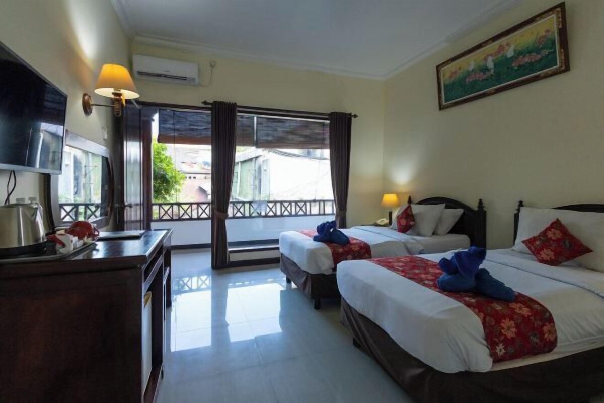 Habitación de hotel con dos camas, televisión, escritorio y balcón con vistas.