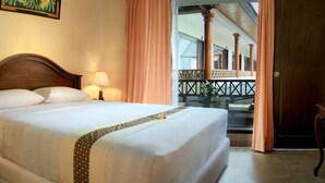 A hotel room with a large bed, a bedside telephone, a television, and a balcony with a railing.