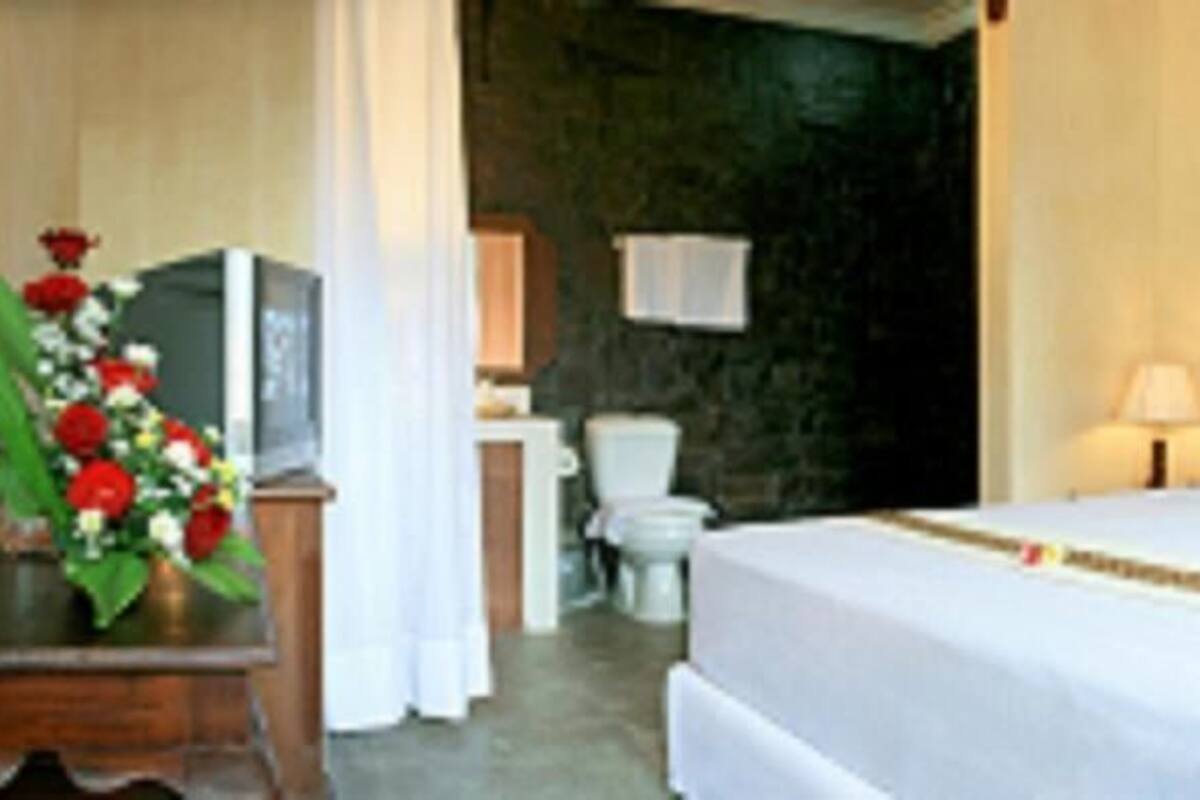 Hotelkamer met een bed, bedlampen, een houten hoofdeinde, een bureau met een bloevas en een badkamer op de achtergrond.
