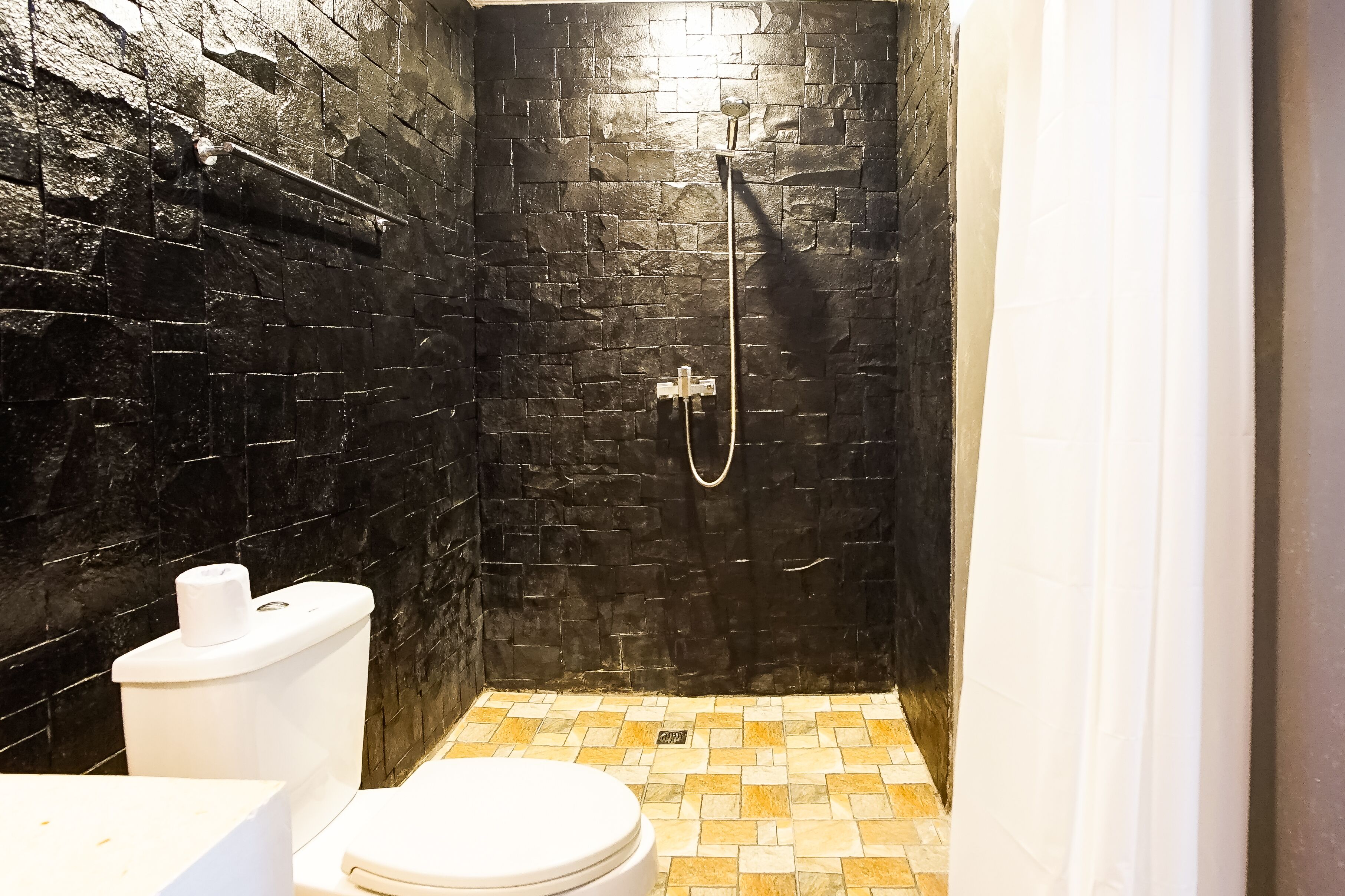 Een badkamer met een douchewand van zwart steen, een wit toilet en een betegelde vloer.