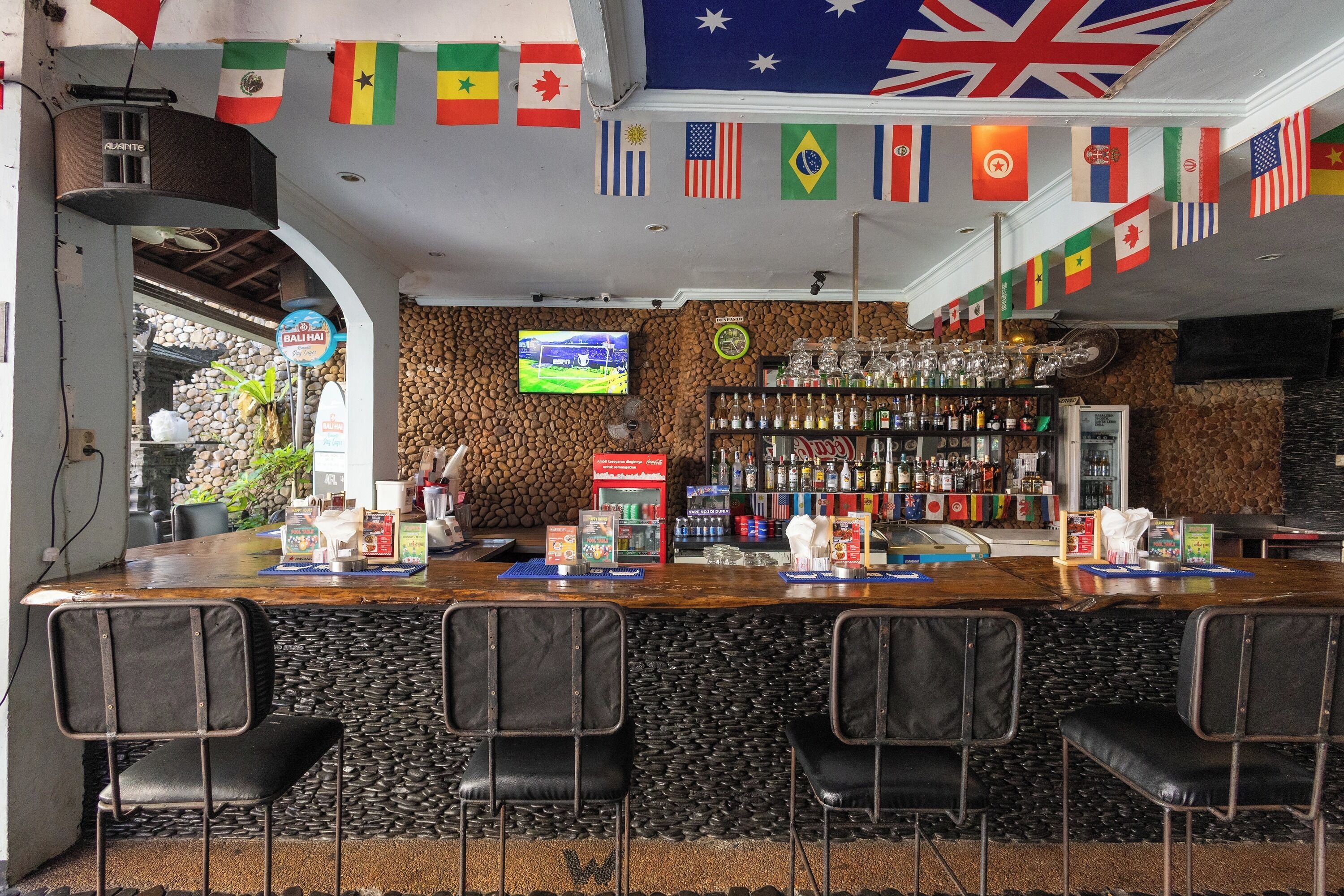 A bar area with a counter, black leather chairs, a television screen, and various flags.