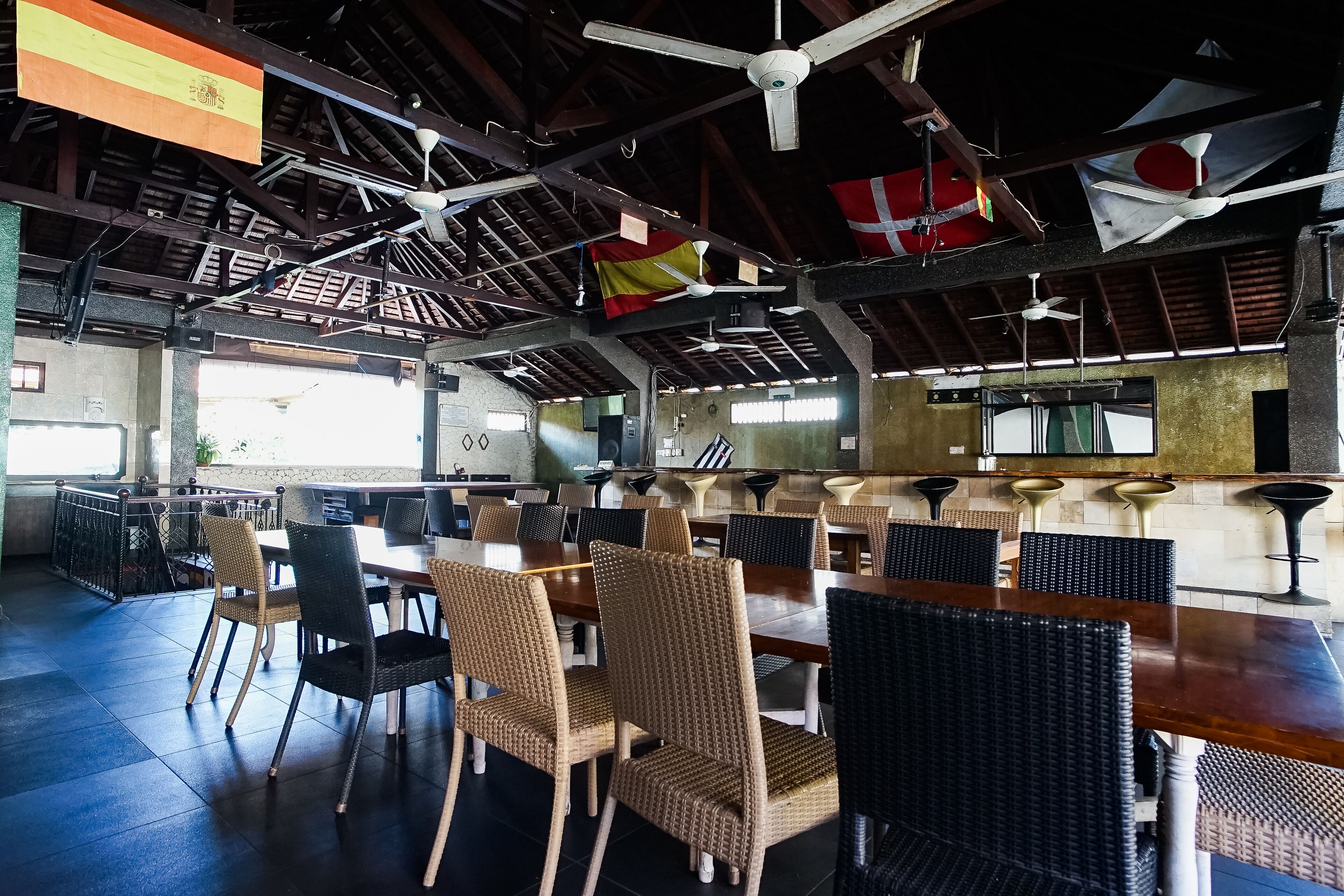 A spacious dining area with high ceilings, multiple ceiling fans, and flags hanging from the beams.