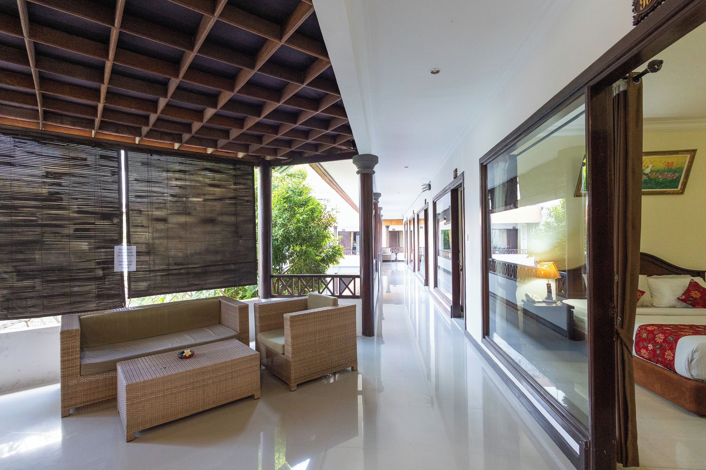 A corridor with wicker furniture, a glass door leading to a bedroom, and a ceiling with a grid pattern.