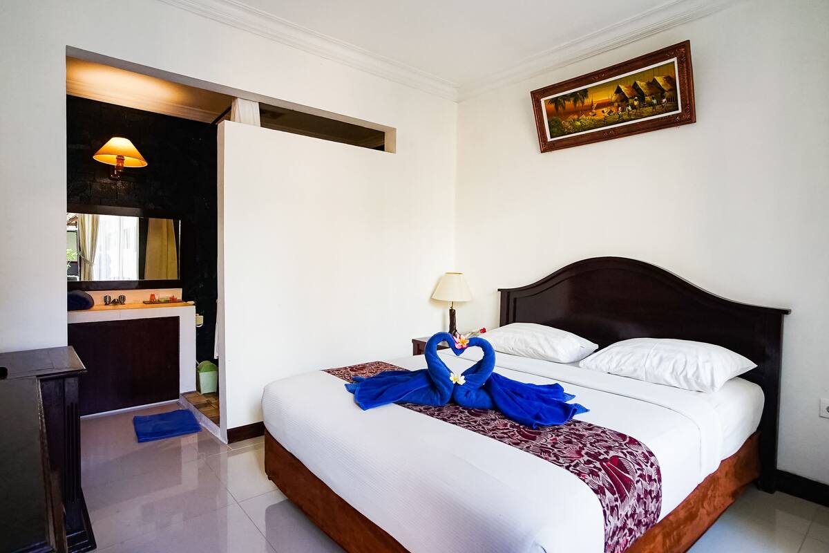 Een hotelkamer met een bed, een bureau, een lamp en een schilderij aan de muur.