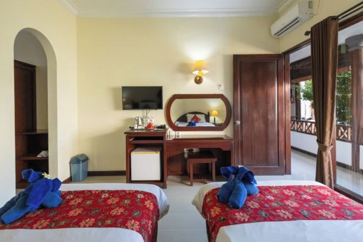 A hotel room with two beds, a desk, a television, and a balcony.