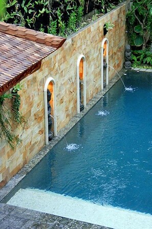 A swimming pool with a stone wall and arched openings. - Taman Ayu Legian Hotel  (Kuta)