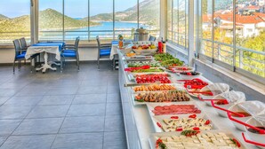 A buffet setup with various food items and a scenic view of a lake and hills. - Kas Artemis Hotel (Kas)