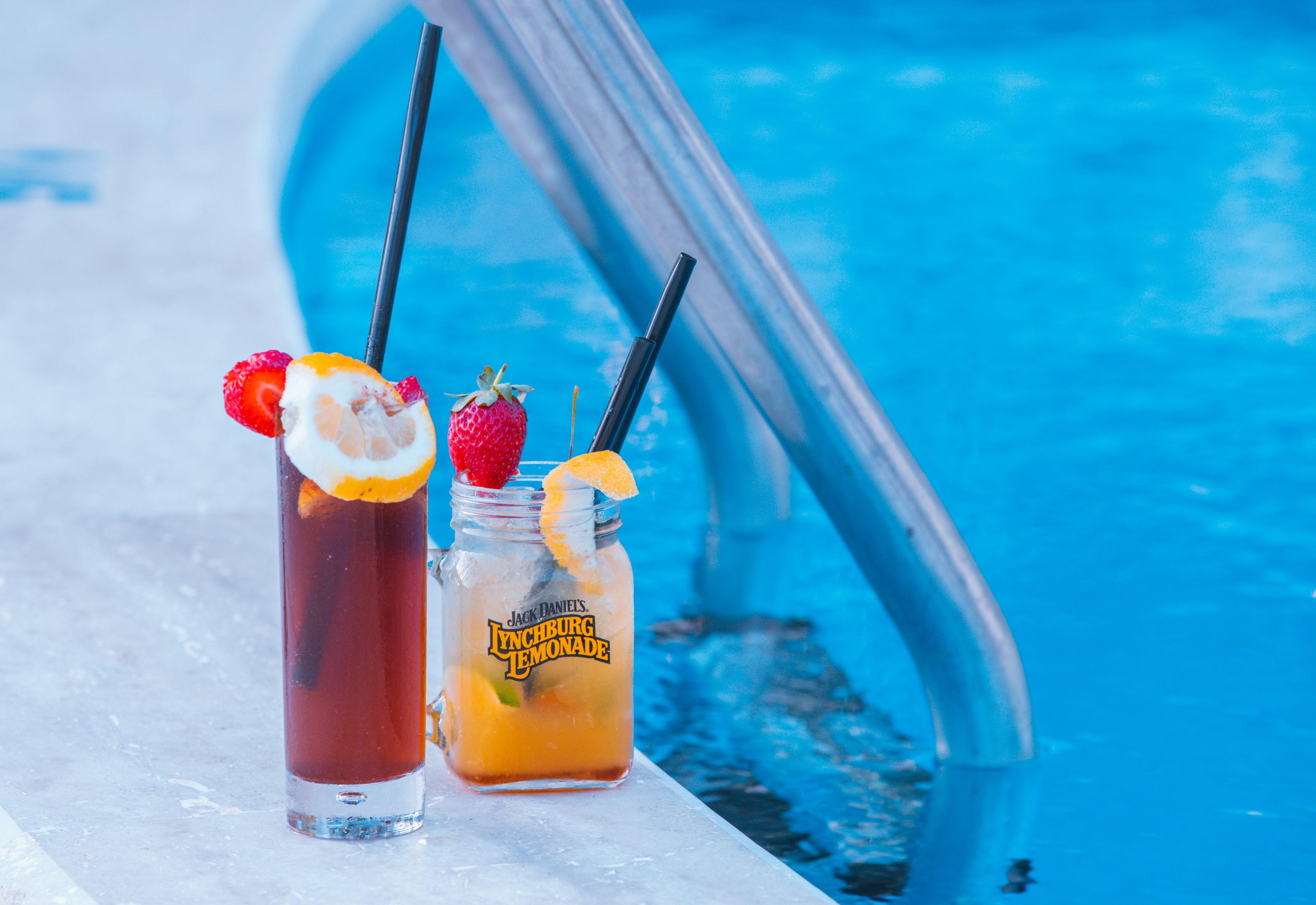 Two drinks with fruit garnishes on a poolside ledge.