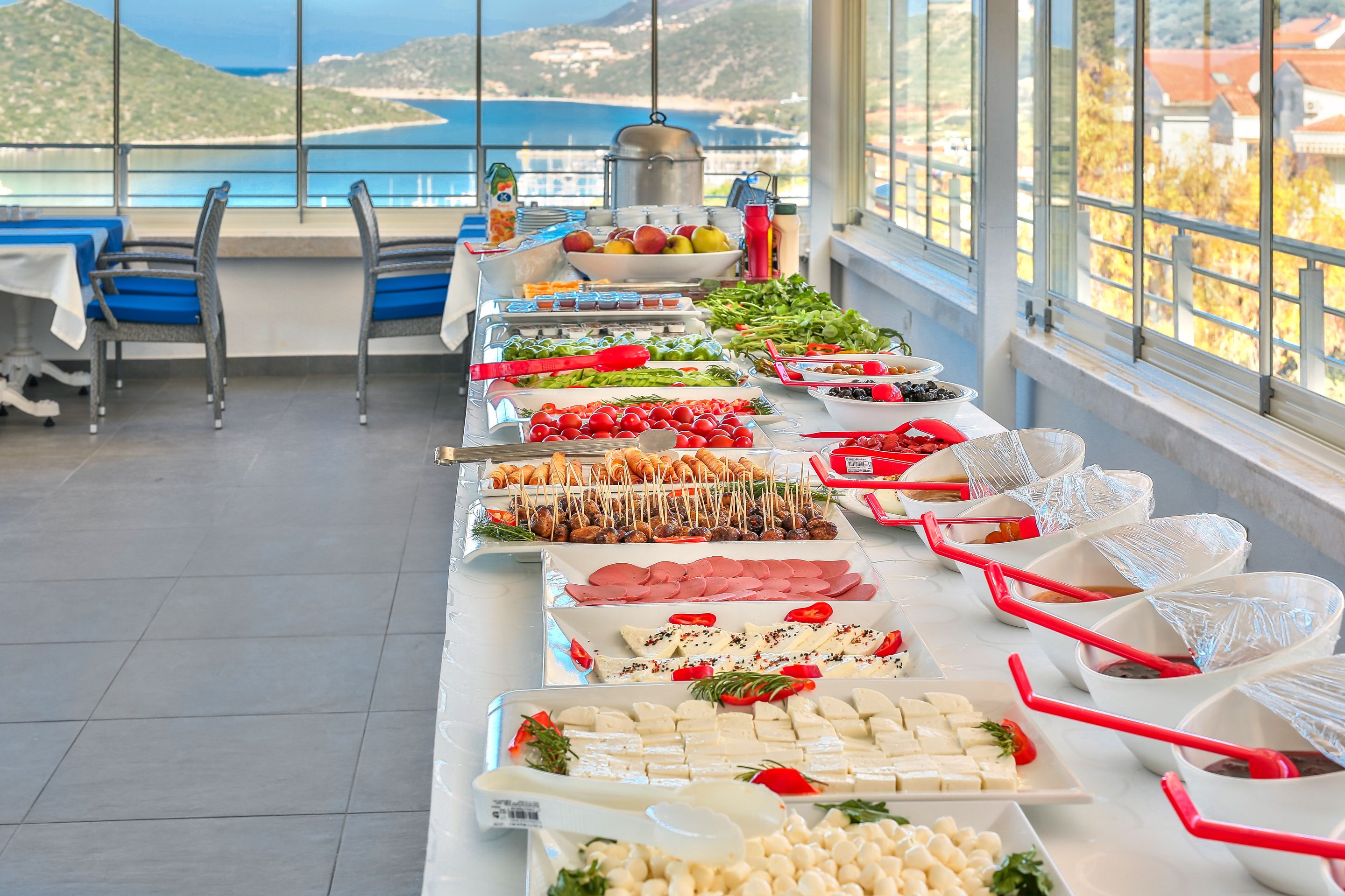 En buffet med diverse retter og et smukt udsigt over havet og bjergene i baggrunden.
