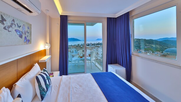 A hotel room with a bed, a balcony with a view of the city, and a large window with curtains. - Kas Artemis Hotel (Kas)