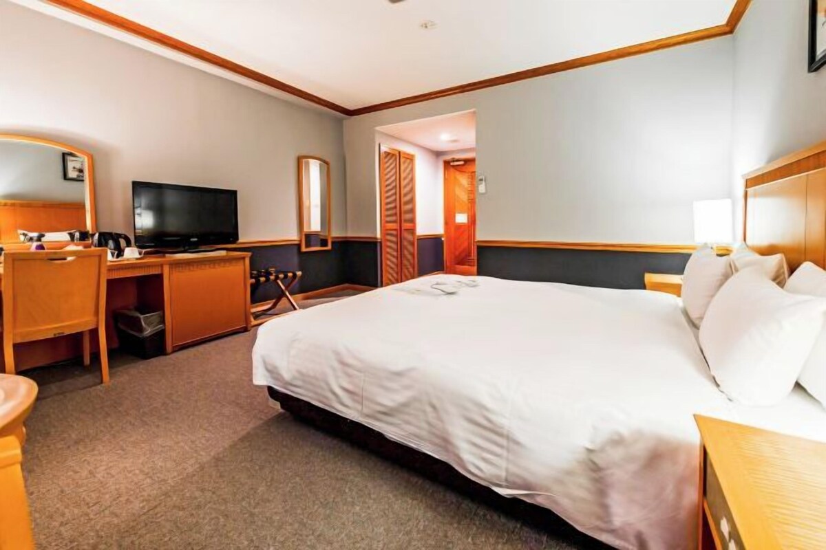 Ett hotellrum med en stor säng, ett skrivbord med en tv, en stol och en garderob.
