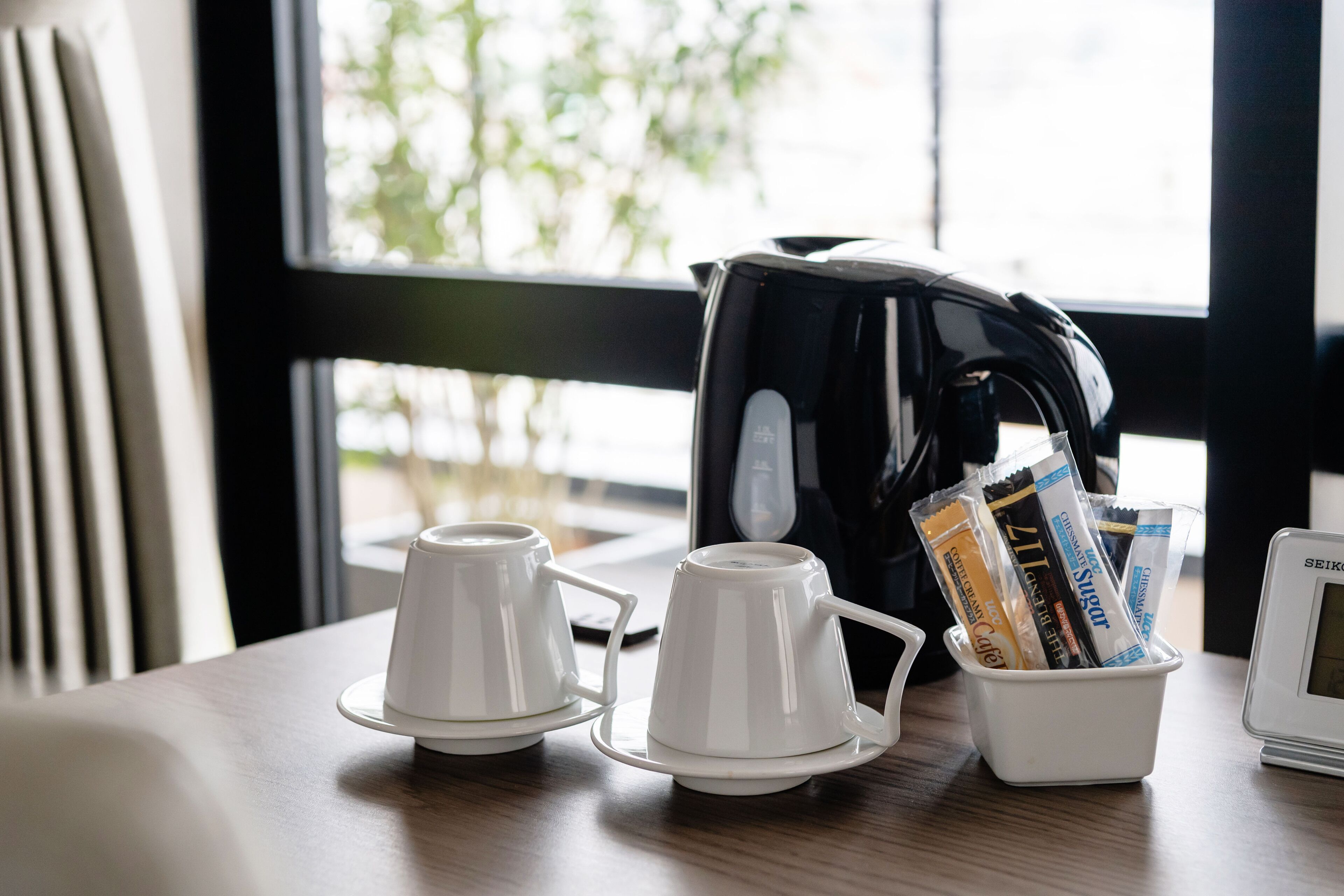 A table with two white cups, a coffee maker, and a container with coffee packets.