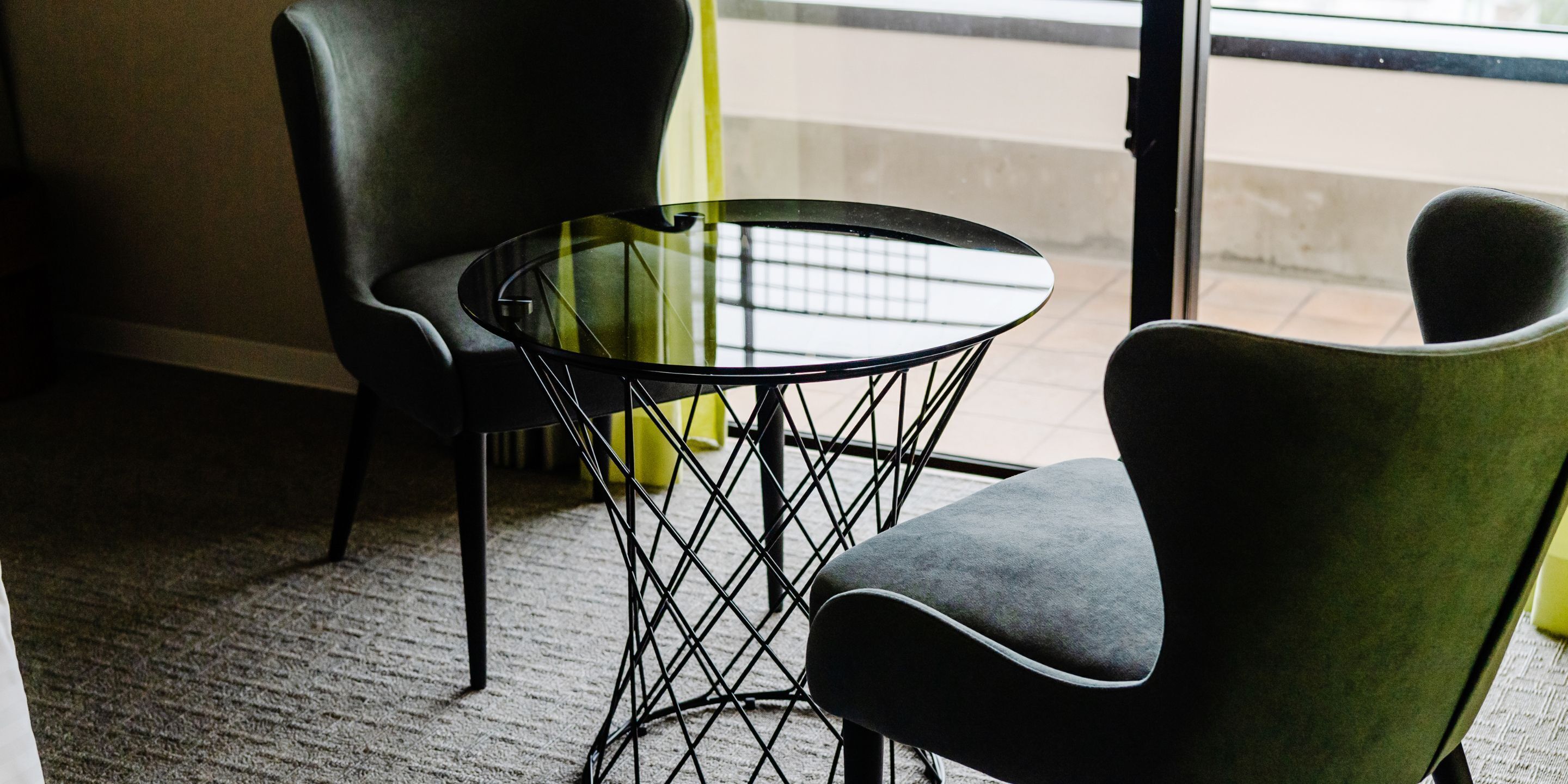 A room with a round glass table and two chairs, one with a curved backrest.