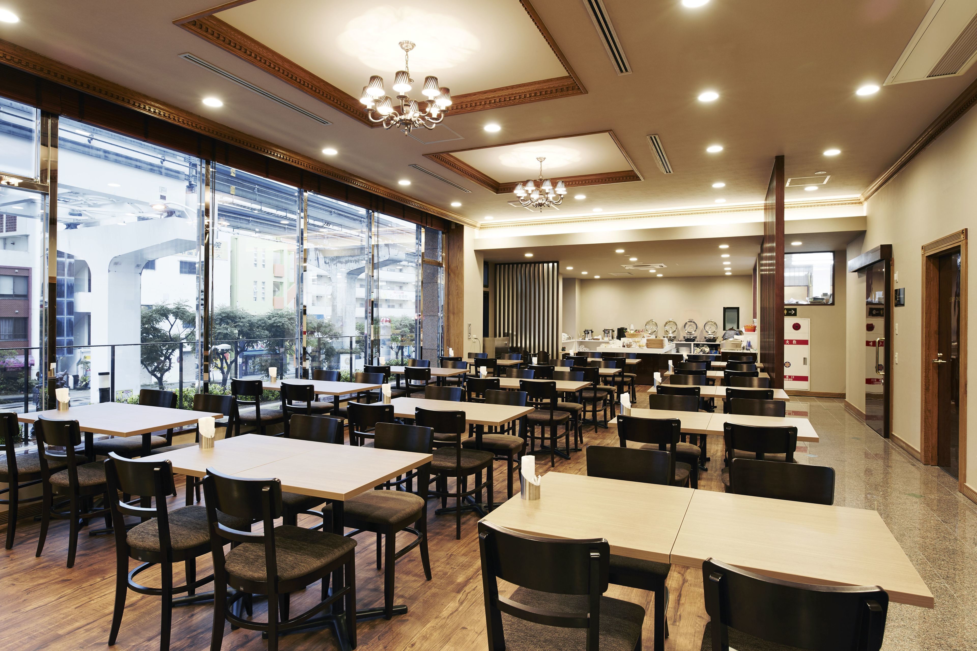 A spacious dining area with multiple tables and chairs, large windows offering a view of the city, and a modern chandelier.