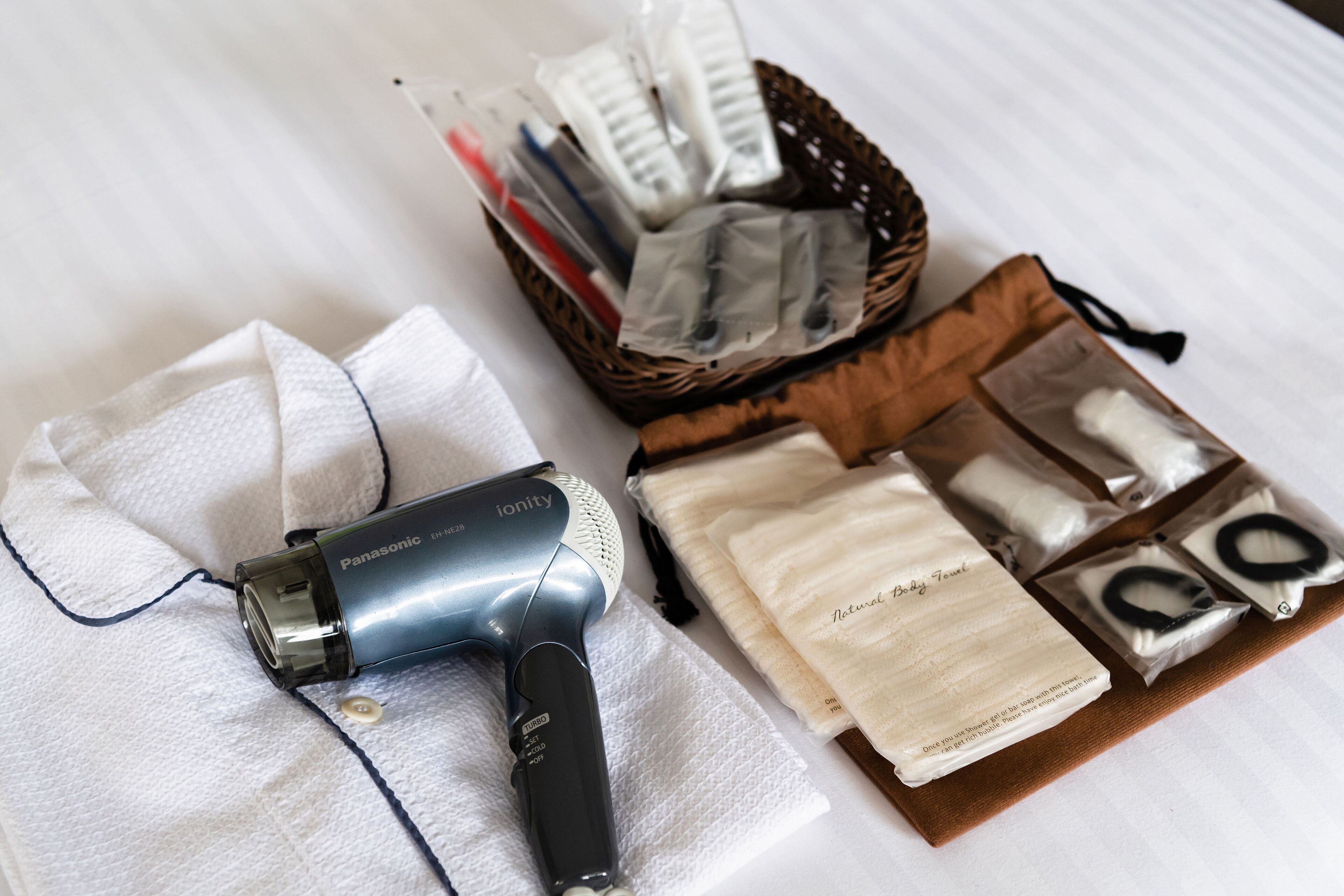 A Panasonic hair dryer, a basket with various hair care products, and a tissue box on a white surface.