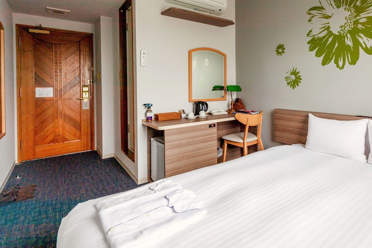 A hotel room with a large bed, a wooden desk, a chair, a mirror, and a wall with a floral decal.