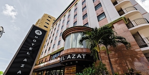 Hotel Azat features a modern design with brick and glass elements, surrounded by lush greenery and palm trees.