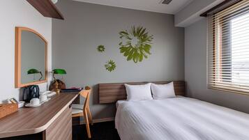 A hotel room with a bed, a desk with a lamp, a chair, a mirror, and wall art.
