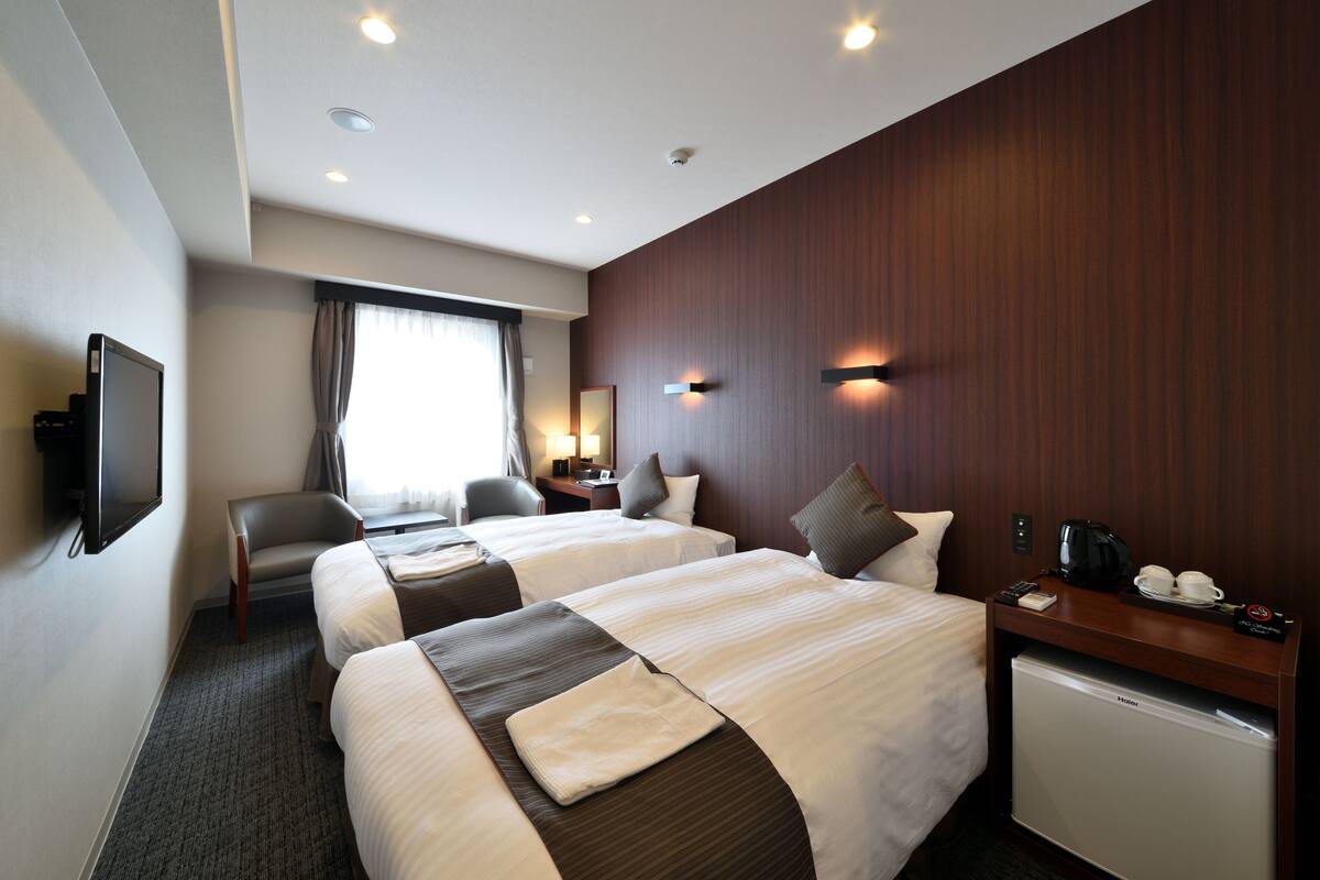 A hotel room with two beds, a desk, a chair, a television, and a mini-fridge.
