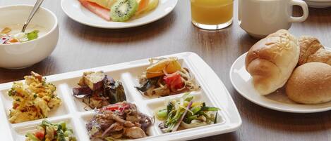 A meal with various dishes including a fruit plate, a glass of orange juice, a cup of coffee, and a plate with rolls and vegetables.