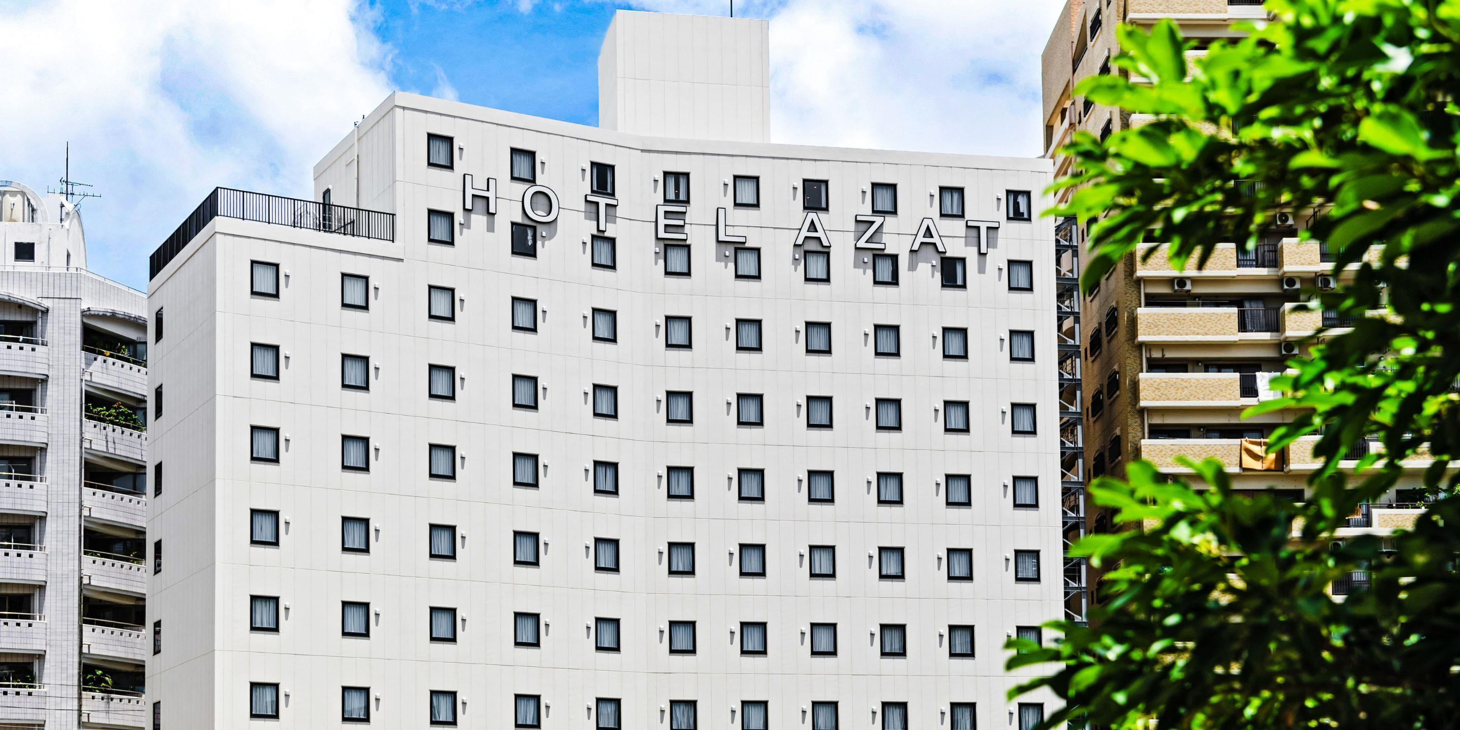 Een meerlaags hotelgebouw met een gelijke gevel, veel ramen en een bord met de tekst 'HOTEL AZAT' bovenop.